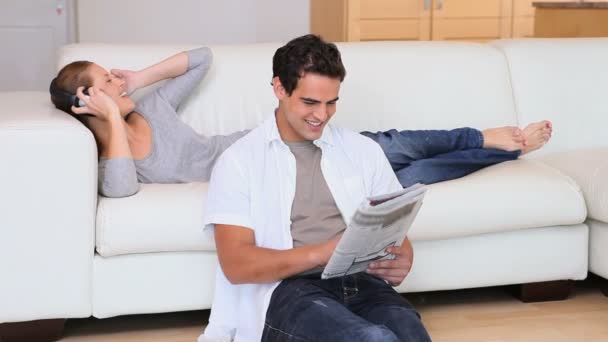 Woman listening to music while her husband reads the newspaper — Stock Video