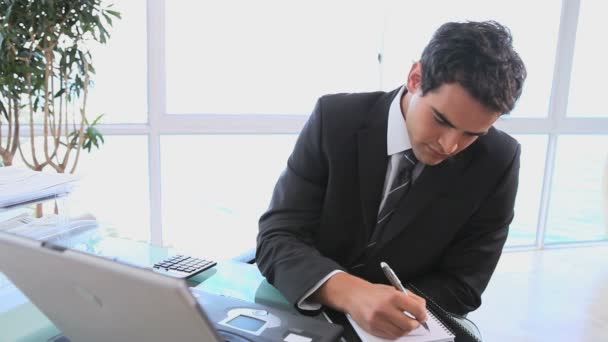 Hombre tomando notas mientras mira su computadora — Vídeos de Stock