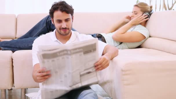 Hombre leyendo un periódico y su novia escucha música — Vídeos de Stock