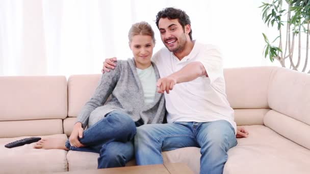 Улыбающаяся пара сидит на диване и смотрит телевизор — стоковое видео