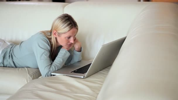 Vrouw die een laptop kijkt op een sofa — Stockvideo