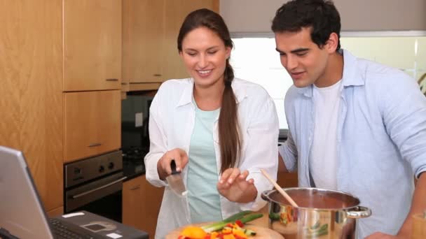 Pareja de cocinar mientras lee la receta en un ordenador portátil — Vídeos de Stock