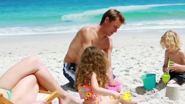 Atya és gyermekei egy homokvárat épület — Stock videók