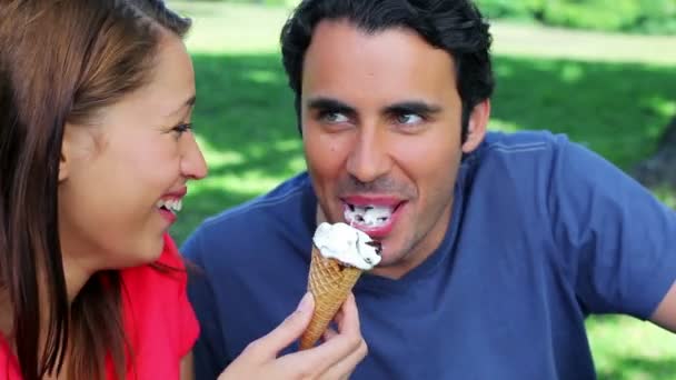 Χαμογελώντας ζευγάρι διατροφικές παγωτά ενώ κάθεται στο γρασίδι — Αρχείο Βίντεο