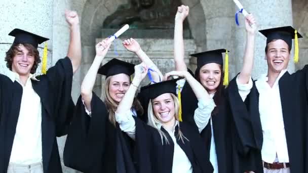 Счастливые выпускники, поднимающие оружие и прыгающие — стоковое видео