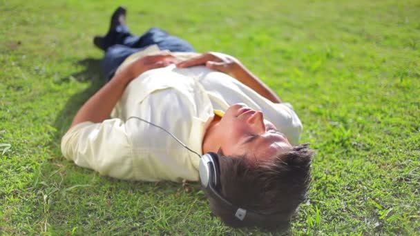 Spokojny człowiek brunetka, leżąc na trawie słuchając muzyki — Wideo stockowe