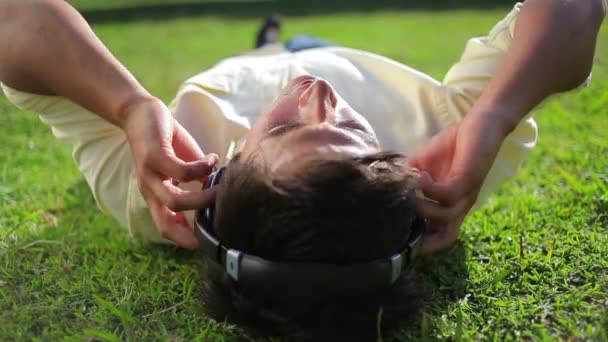 Fredlig man lyssnar på musik liggande i gräset — Stockvideo