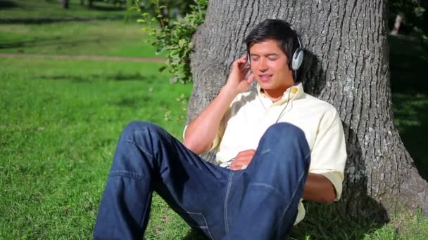 Friedlicher Mann lehnt sich beim Musikhören an einen Baum — Stockvideo