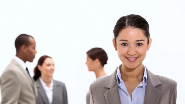 Mujer de negocios sonriente con compañeros de trabajo detrás de ella — Vídeos de Stock