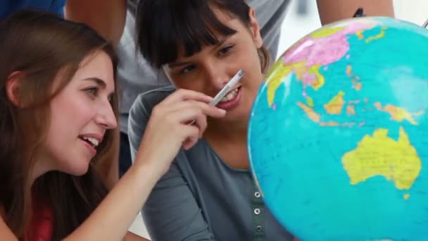 Улыбающиеся студенты указывают на страны на глобусе — стоковое видео