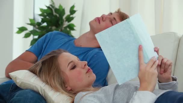 Mujer leyendo un libro mientras su novio está durmiendo la siesta — Vídeos de Stock