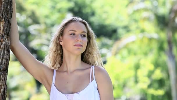 Mujer sonriente apoyada en un árbol — Vídeos de Stock