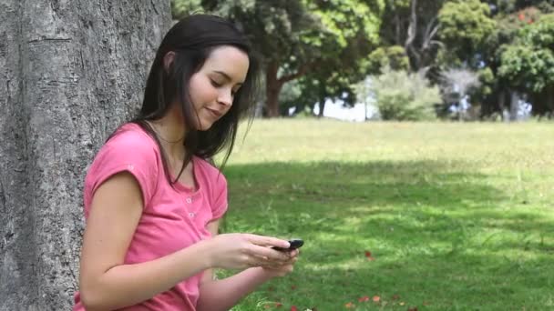 Lachende vrouw met behulp van een mobiele telefoon in een park — Stockvideo