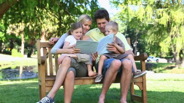 Rodina sedí na lavičce, čtení knihy — Stock video