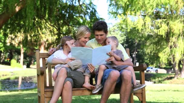 Familie liest ein Buch, während sie auf einer Bank sitzt — Stockvideo