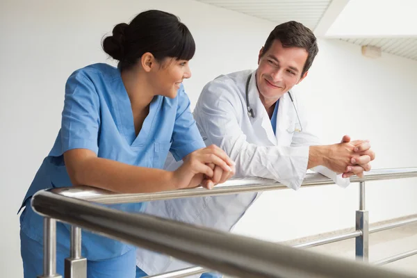 Médico e enfermeiro sorrindo e inclinando-se contra o trilho — Fotografia de Stock