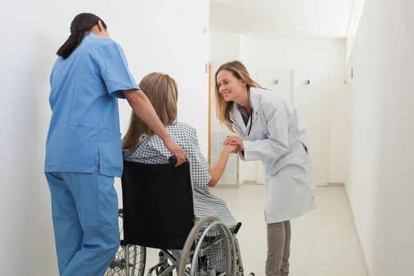 Médico conversando com paciente em cadeira de rodas enquanto enfermeira está empurrando — Fotografia de Stock