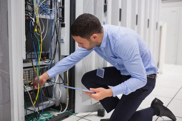 Hombre comprobación de PC tableta como él está conectando los cables en el servidor — Foto de Stock