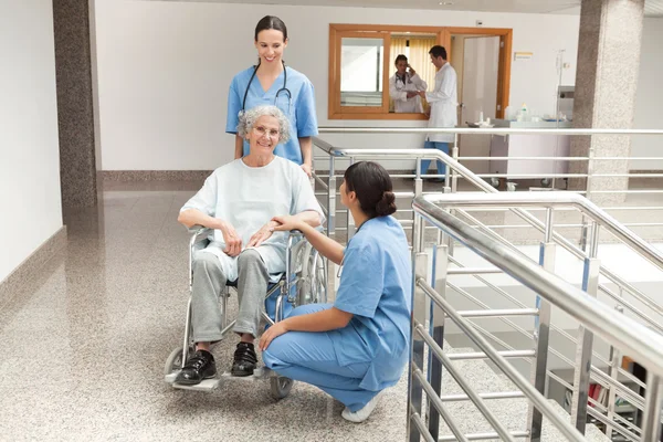 Two nurses looking after old women sitting in wheelchair — Stock Photo, Image