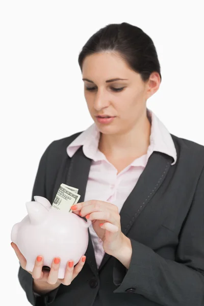 Brunette putting dollars into a piggy-bank — Stock Photo, Image