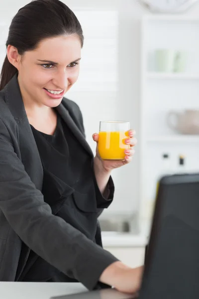 Mulher segurando um copo de suco enquanto olha para um laptop — Fotografia de Stock