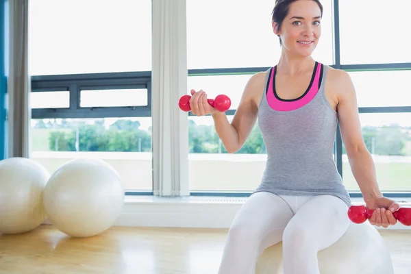 Glückliche Frau stemmt Gewichte auf dem Gymnastikball — Stockfoto