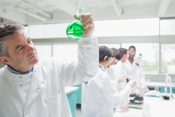 Man som tittar på vätska medan andra kemister gör forskning — Stockfoto