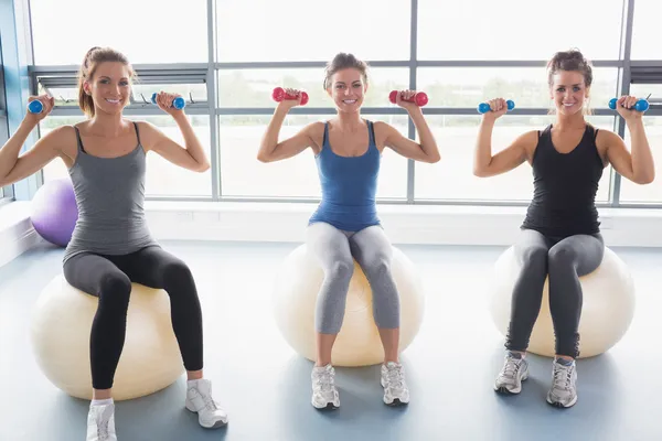 Три улыбающиеся женщины сидят на мячах для упражнений и поднимают вес — стоковое фото