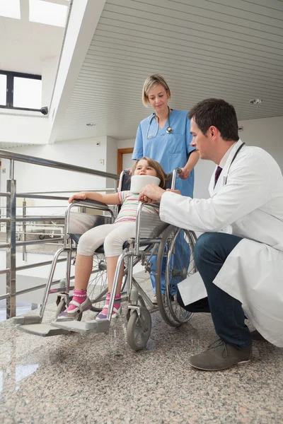 Doctor crouching next to child in wheelchair with nurse pushing — Stock Photo, Image