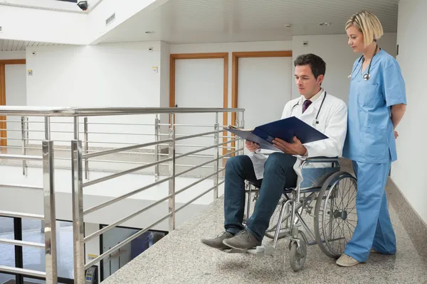 Médico sentado em cadeira de rodas examinando notas com enfermeira — Fotografia de Stock