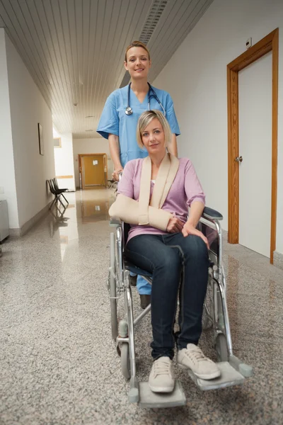 Nurse pushing wheelchair of patient with arm sling — Stock Photo, Image