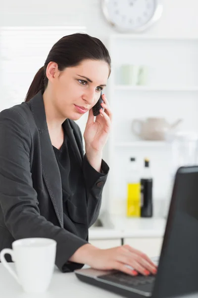 Donna che tiene un telefono cellulare mentre utilizza un computer portatile — Foto Stock