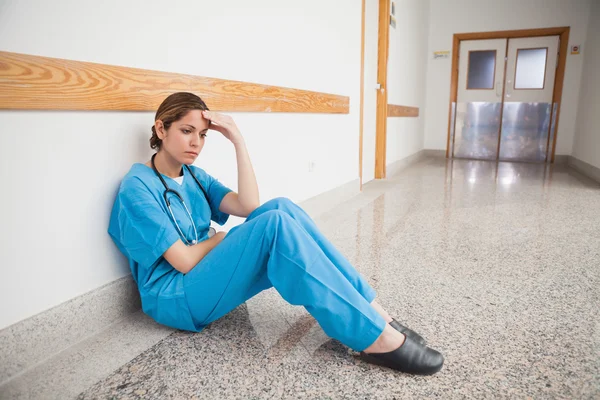 Медсестра сидит на полу рукой на лбу — стоковое фото