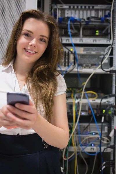 Mulher sorridente com smartphone na frente dos servidores — Fotografia de Stock