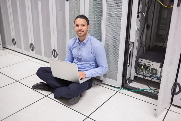 Man sitting beside servers with laptop — Stock Photo, Image