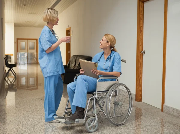 Nurse with drink talking to nurse in wheelchair with folder — Stock Photo, Image