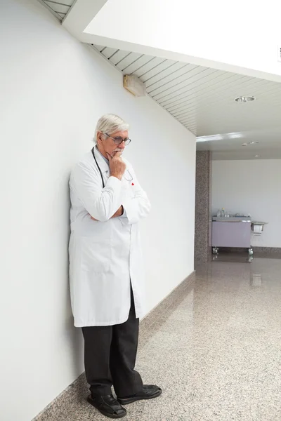 Thinking doctor leaning against wall — Stock Photo, Image