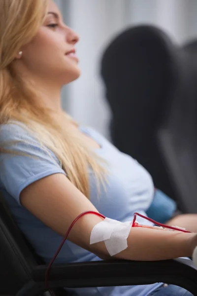 Улыбающаяся женщина получает переливание крови и сидит на стуле — стоковое фото