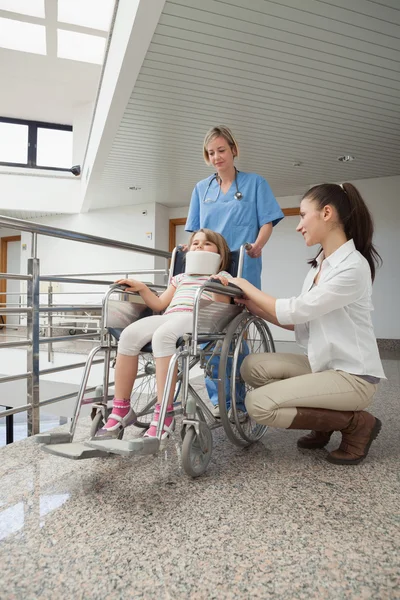 Mère accroupie à côté de son enfant en fauteuil roulant avec poussée infirmière — Photo