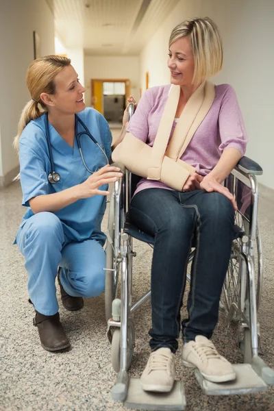 Enfermeira conversando com paciente em cadeira de rodas com braço em funda — Fotografia de Stock