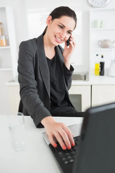 Sorrindo mulher chamando ao usar um laptop — Fotografia de Stock