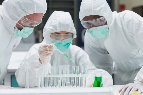 Chemist adding green liquid to test tubes with two other chemist — Stock Photo, Image