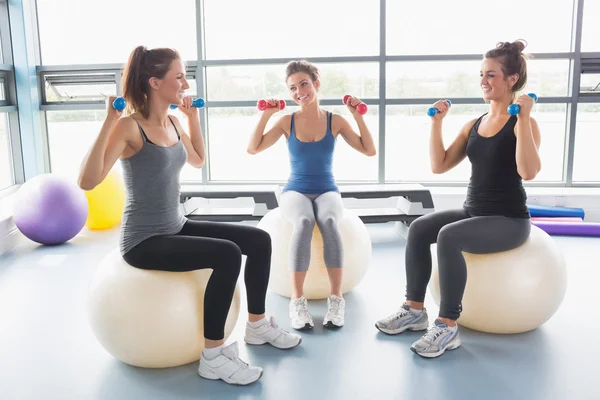 Três mulheres levantando pesos em bolas de exercício — Fotografia de Stock