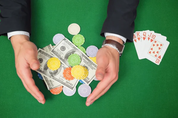 Hands grabbing dollars and chips from table beside royal flush — Stock Photo, Image