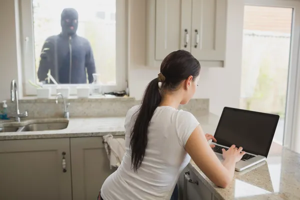 Räuber sieht Frau mit Laptop durch Fenster an — Stockfoto