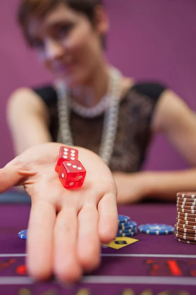Woman sitting at table while holding dices — Stock Photo, Image