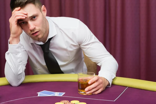 Homem apoiado na mesa de poker bebendo uísque — Fotografia de Stock