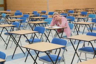 Student sitting at desk in empty exam hall clipart