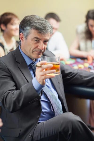 Hombre con puro levantando vaso de whisky en la mesa de ruleta — Foto de Stock