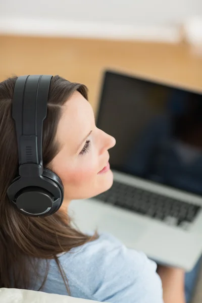 Mujer escuchando música con su portátil en el sofá —  Fotos de Stock